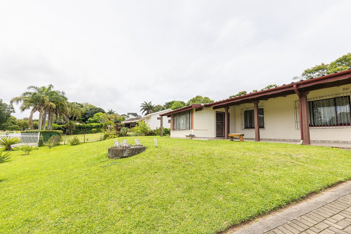 A view of the rear exterior of the house featuring a covered patio, security bars on windows, and a spacious lawn area.