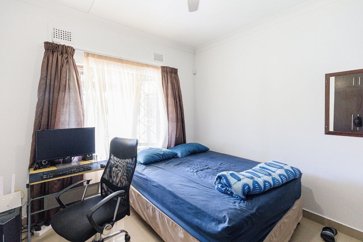 A functional bedroom featuring tiled flooring, a ceiling fan, and security bars on the window, providing a practical and secure living space.