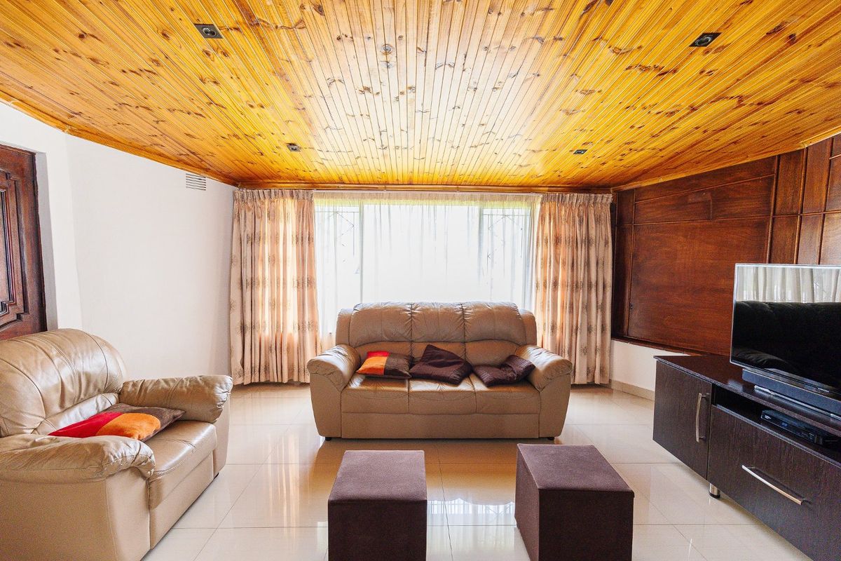 A living room featuring a distinctive timber tongue and groove ceiling, tiled flooring, and wood-paneled accent wall.