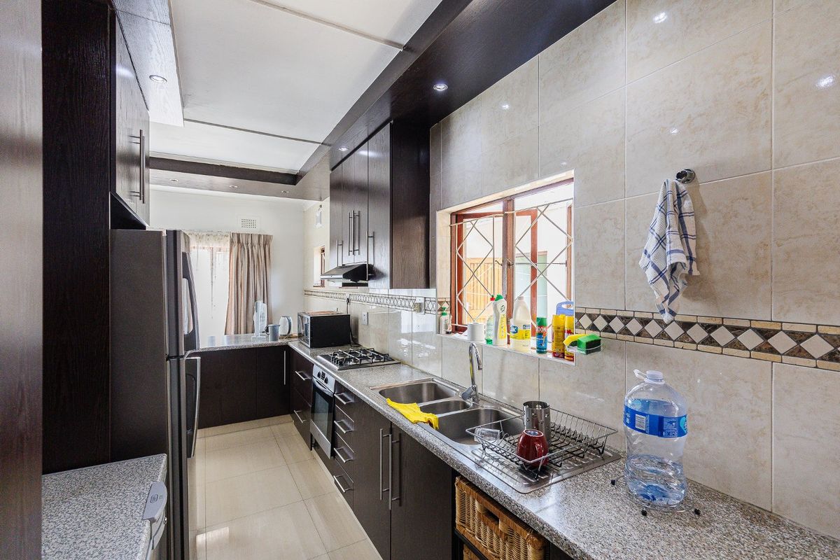 A functional kitchen featuring dark wood cabinetry, granite countertops, a stainless steel double sink, and built-in appliances including a gas hob and oven.