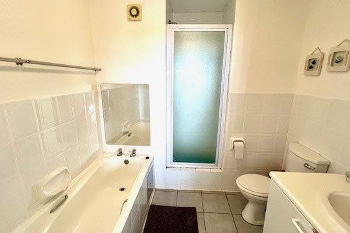 A functional bathroom featuring a bathtub, separate shower enclosure, toilet, and vanity basin with tiled splashbacks.
