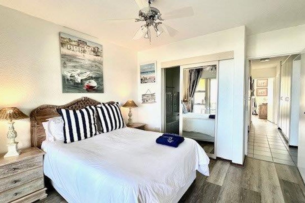A bedroom featuring a ceiling fan, mirrored sliding door wardrobe, and laminate flooring, with an adjacent hallway visible.