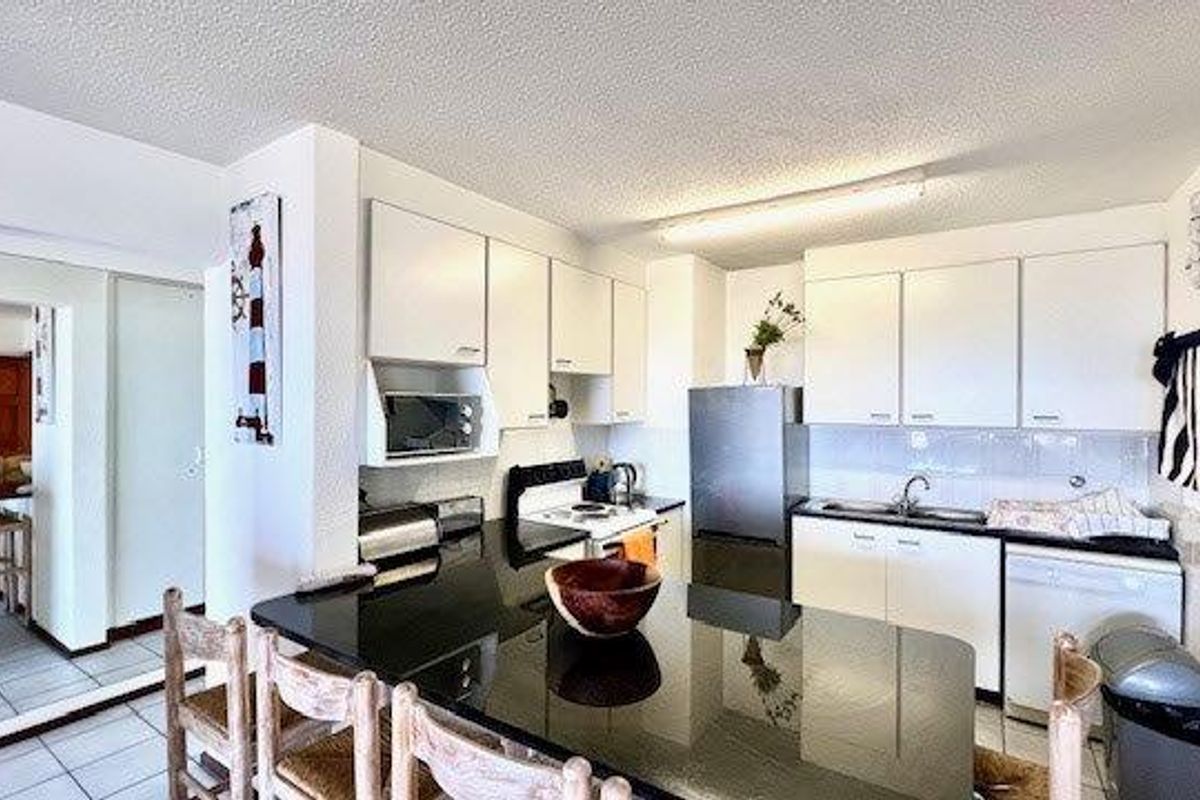 A functional kitchen featuring white cabinetry, black granite countertops, and integrated appliances, with an adjacent breakfast bar area.