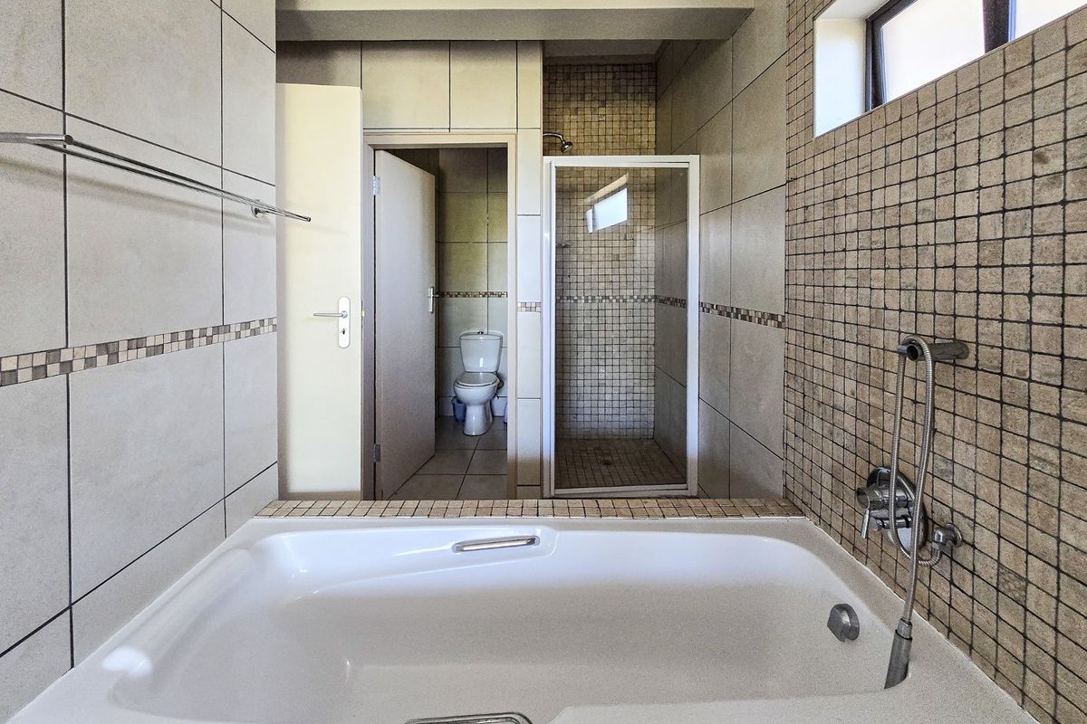 A functional bathroom featuring a built-in bathtub, separate shower enclosure, and a private toilet area with neutral wall tiling.