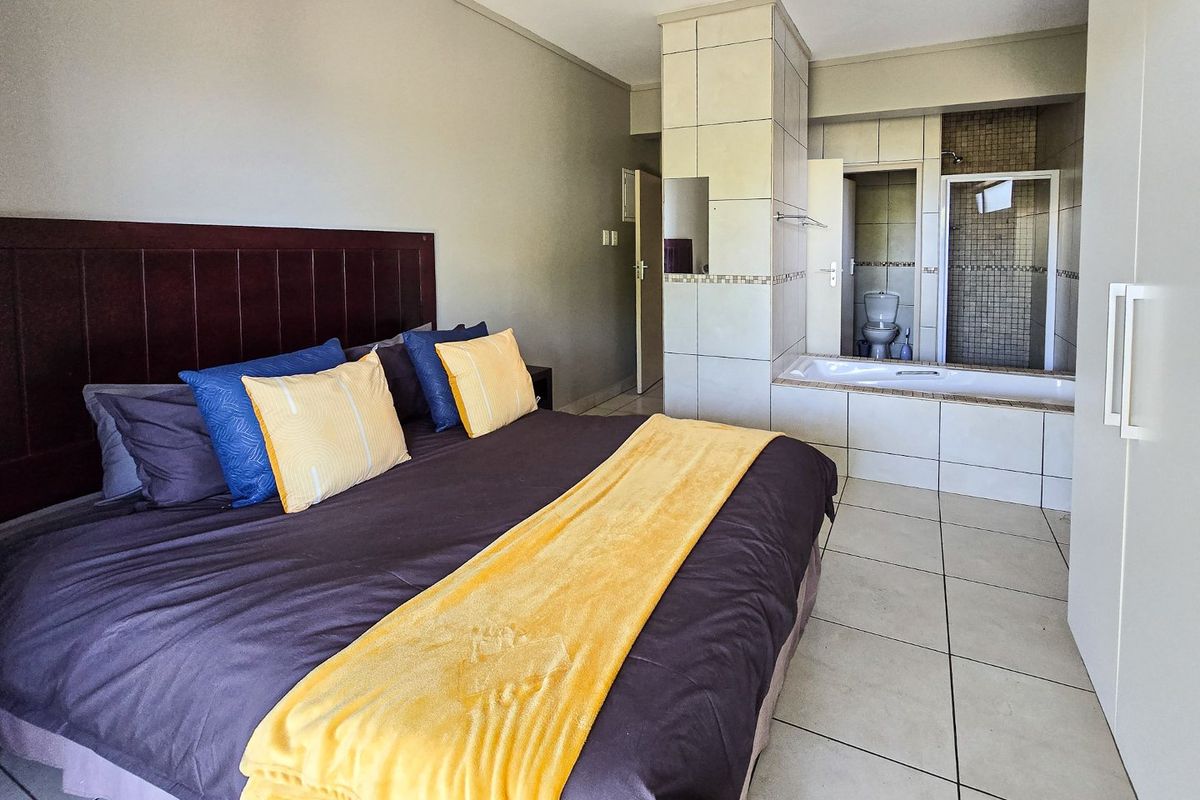 Spacious bedroom featuring an open-plan en-suite bathroom with a built-in bathtub, glass shower enclosure, and tiled finishes throughout.