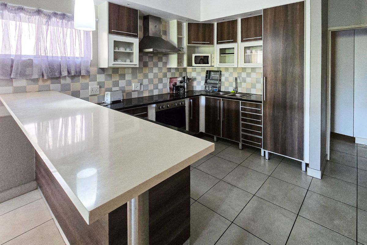 Modern kitchen featuring a stone breakfast bar, dark wood-finish cabinetry, stainless steel appliances, and a neutral tiled backsplash.
