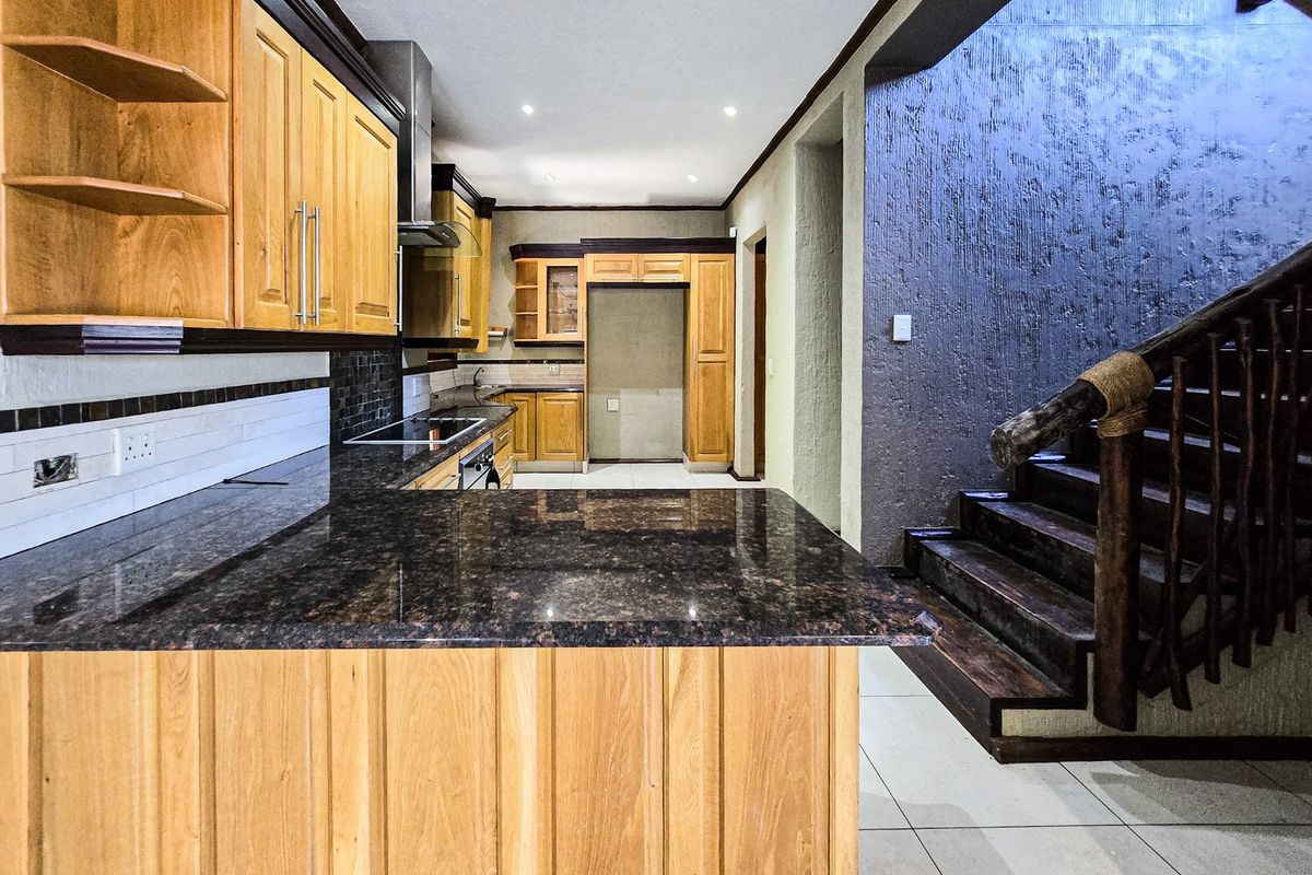Spacious kitchen featuring granite countertops, wooden cabinetry, and integrated appliances, adjacent to a staircase with a rustic wooden balustrade.