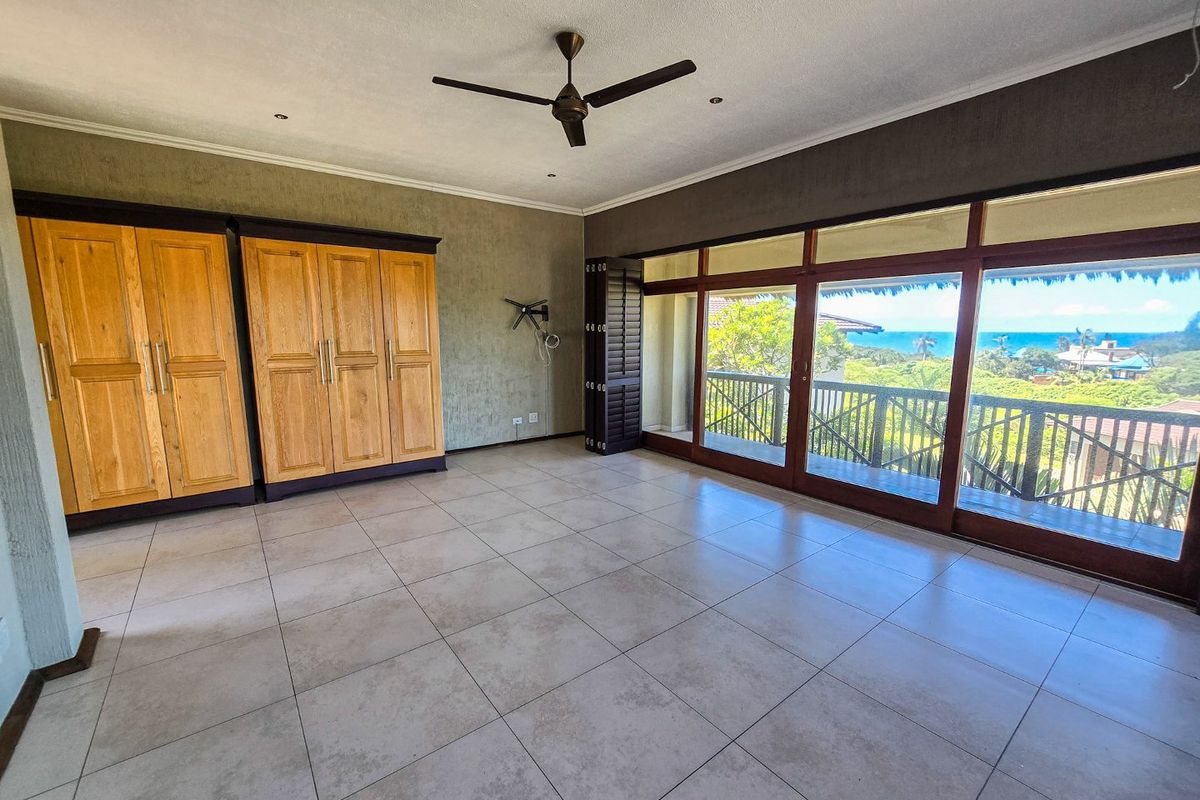 Spacious bedroom featuring built-in wooden wardrobes, tiled flooring, and large sliding glass doors opening to a balcony with scenic coastal views.