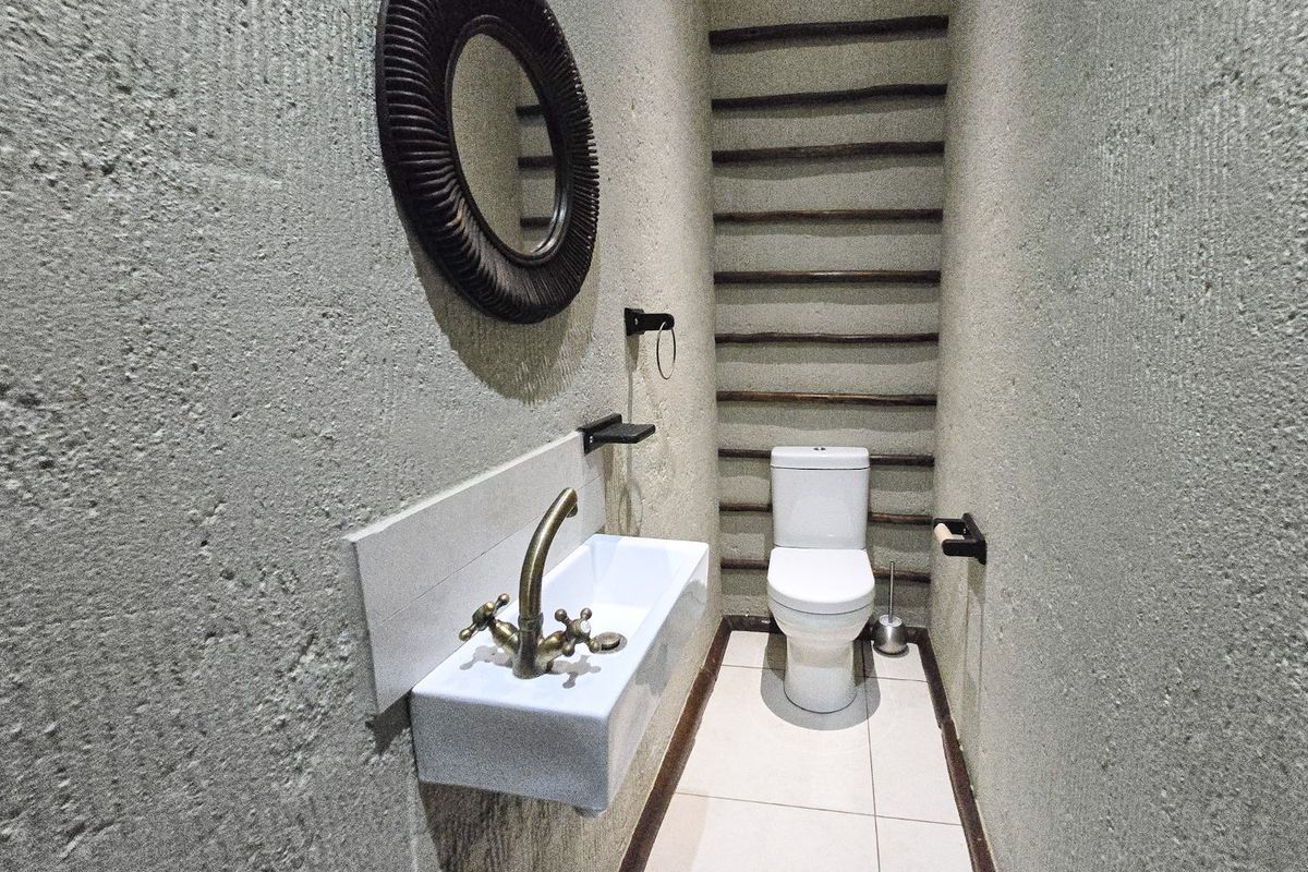 A compact, modern guest bathroom featuring a wall-mounted basin with brass fixtures, a toilet, and a unique textured wall with timber slat detailing.