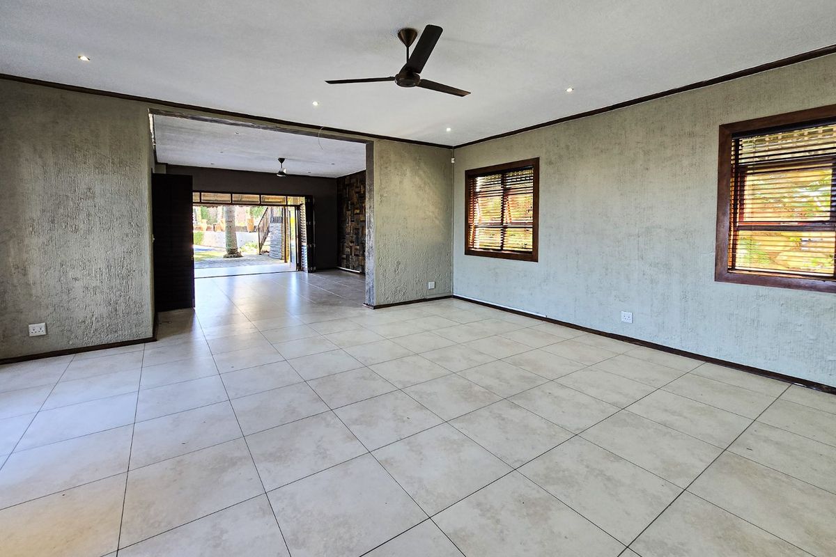 Spacious, open-plan living area featuring neutral tiled flooring, textured walls, recessed lighting, and a ceiling fan, with seamless flow to an outdoor patio space.
