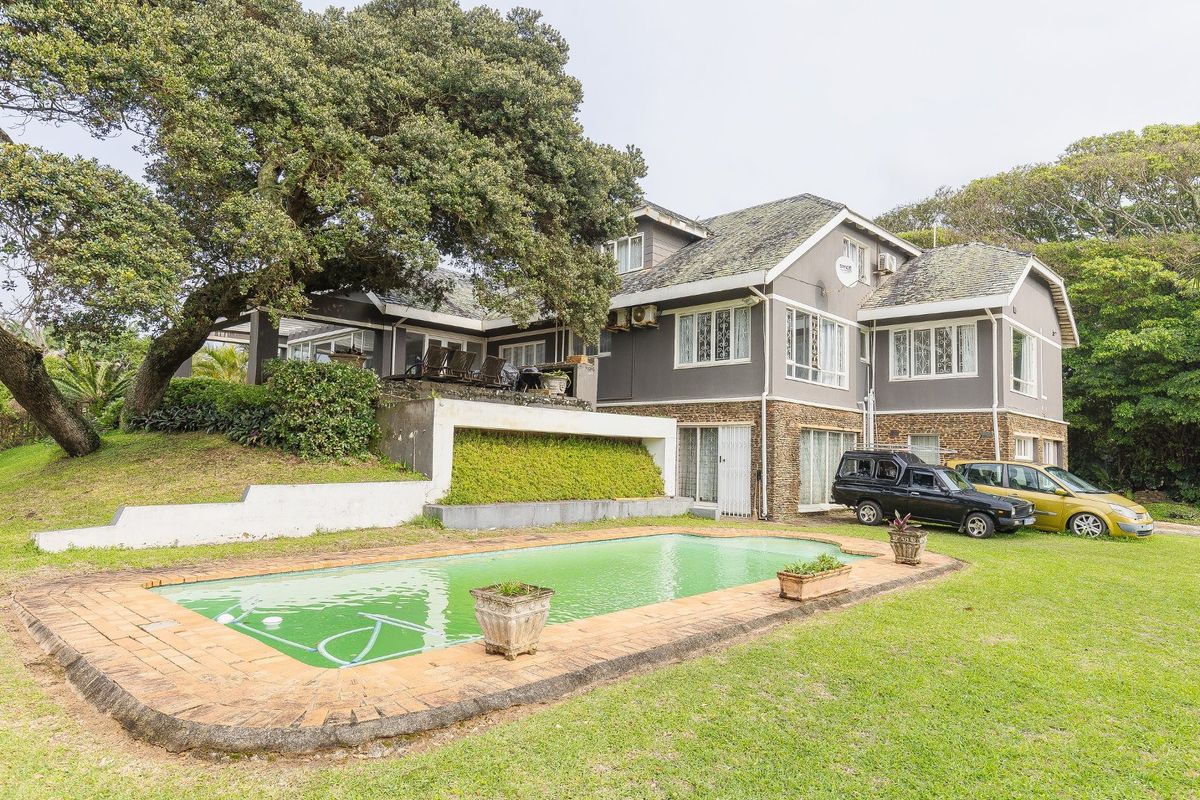 Rear view of a multi-story house featuring a swimming pool, stone-clad exterior walls, and a large mature tree in the garden.