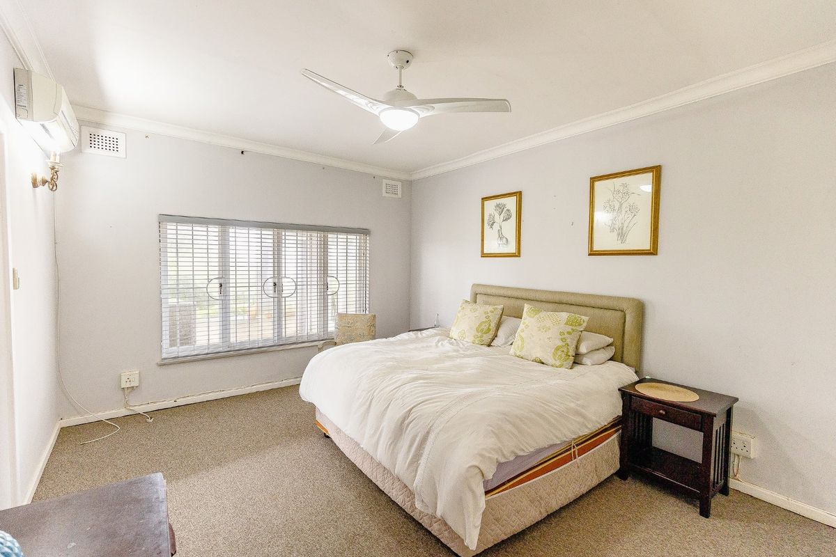A spacious bedroom featuring neutral walls, carpeted flooring, a ceiling fan, and a split-system air conditioner for climate control.