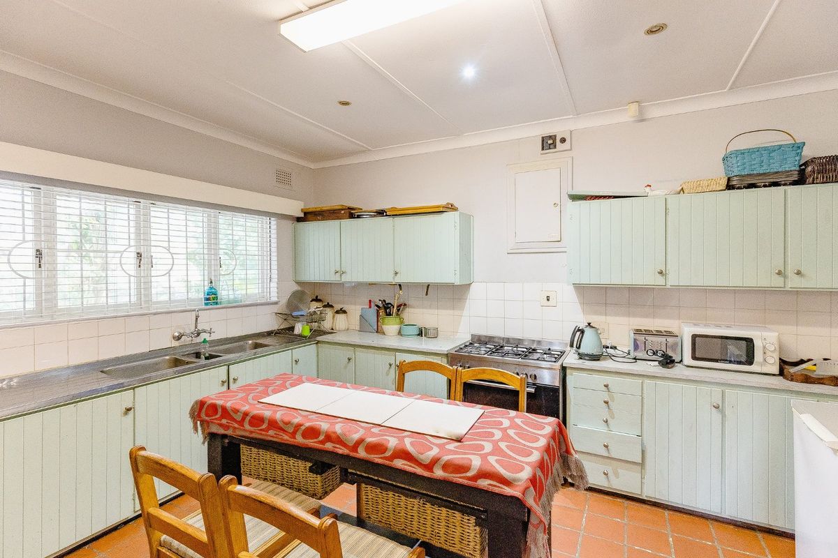 A functional kitchen featuring dated cabinetry, a gas stove, stainless steel sink, and terracotta floor tiles, offering potential for a modern renovation.