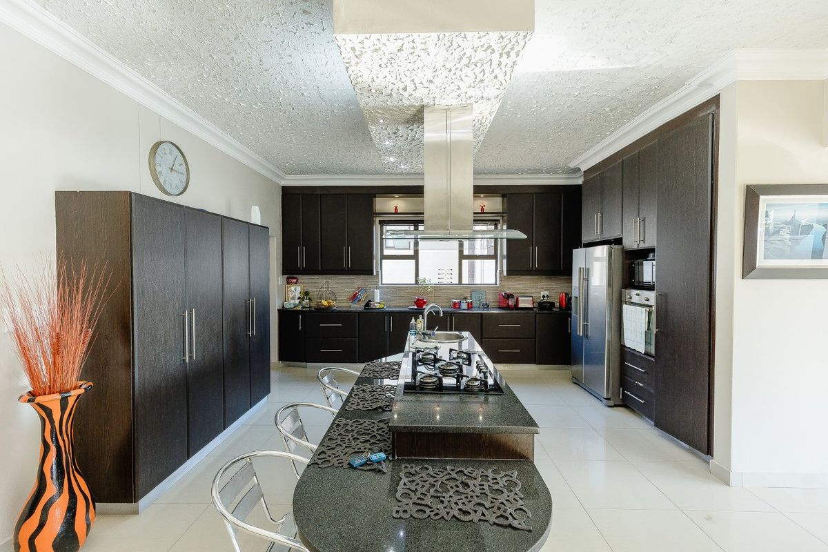 Modern kitchen featuring dark wood cabinetry, granite countertops, a central island with a gas hob, and integrated stainless steel appliances.