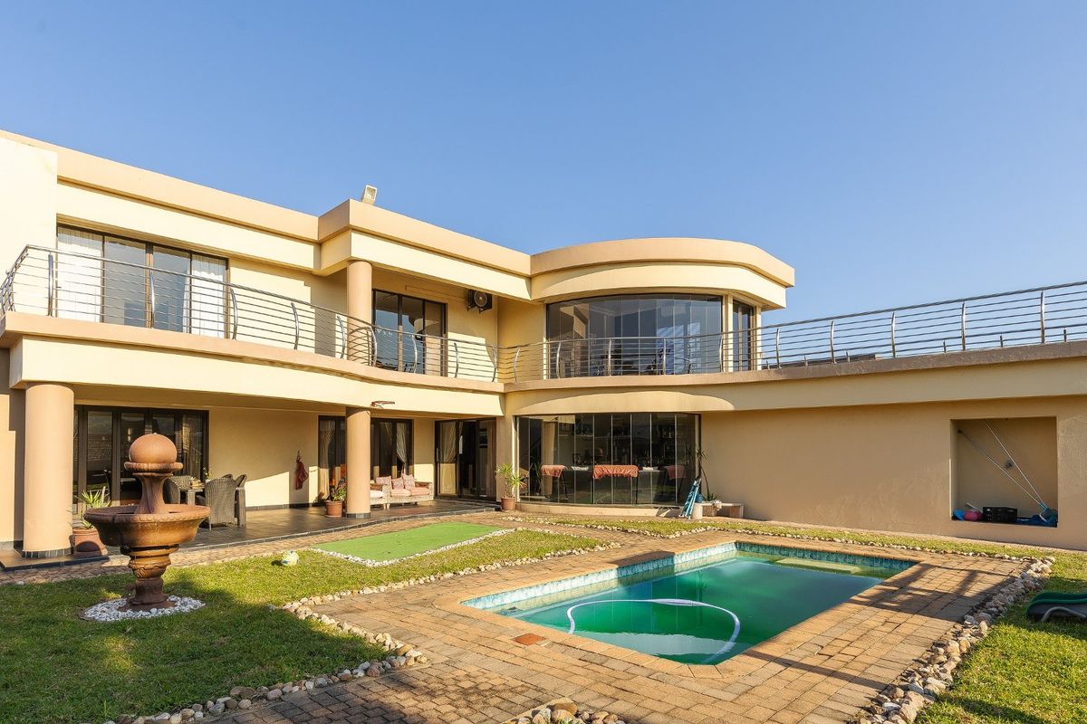 Rear view of a two-story residence featuring a swimming pool, paved deck, covered patio, and an upper-level balcony with stainless steel railings.
