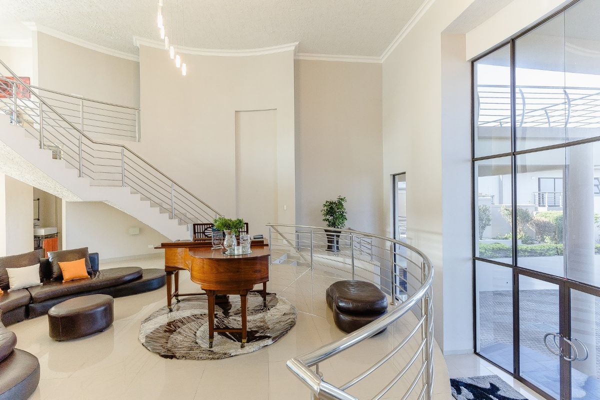 Spacious open-plan living area featuring a grand staircase with stainless steel balustrades, high ceilings, and large windows providing ample natural light.