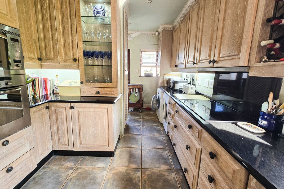 A galley-style kitchen featuring light oak cabinetry, black granite countertops, integrated appliances, and ceramic tile flooring with a dedicated laundry area.