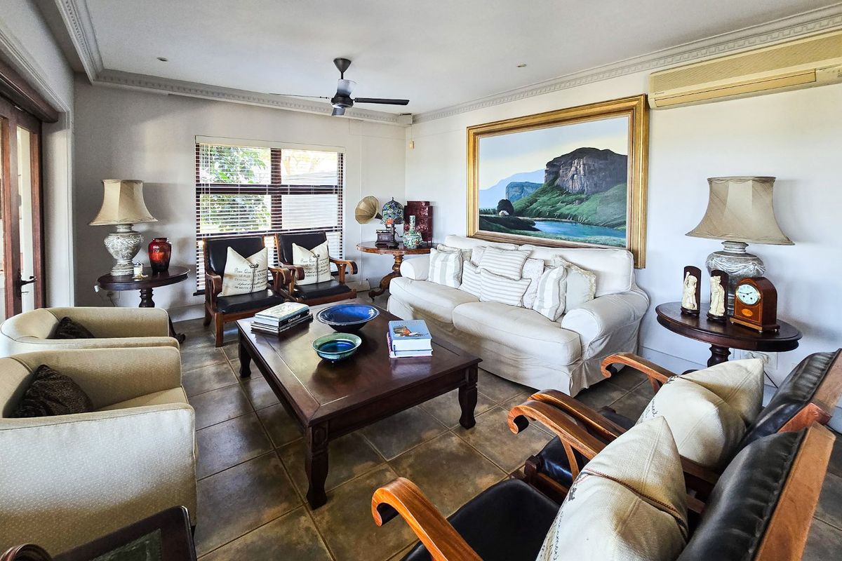 A spacious living room featuring tiled flooring, crown molding, a ceiling fan, and a wall-mounted split-system air conditioner.