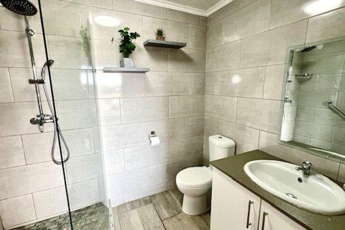 Modern bathroom featuring a walk-in shower with glass screen, vanity cabinet with integrated sink, and neutral wall tiling.