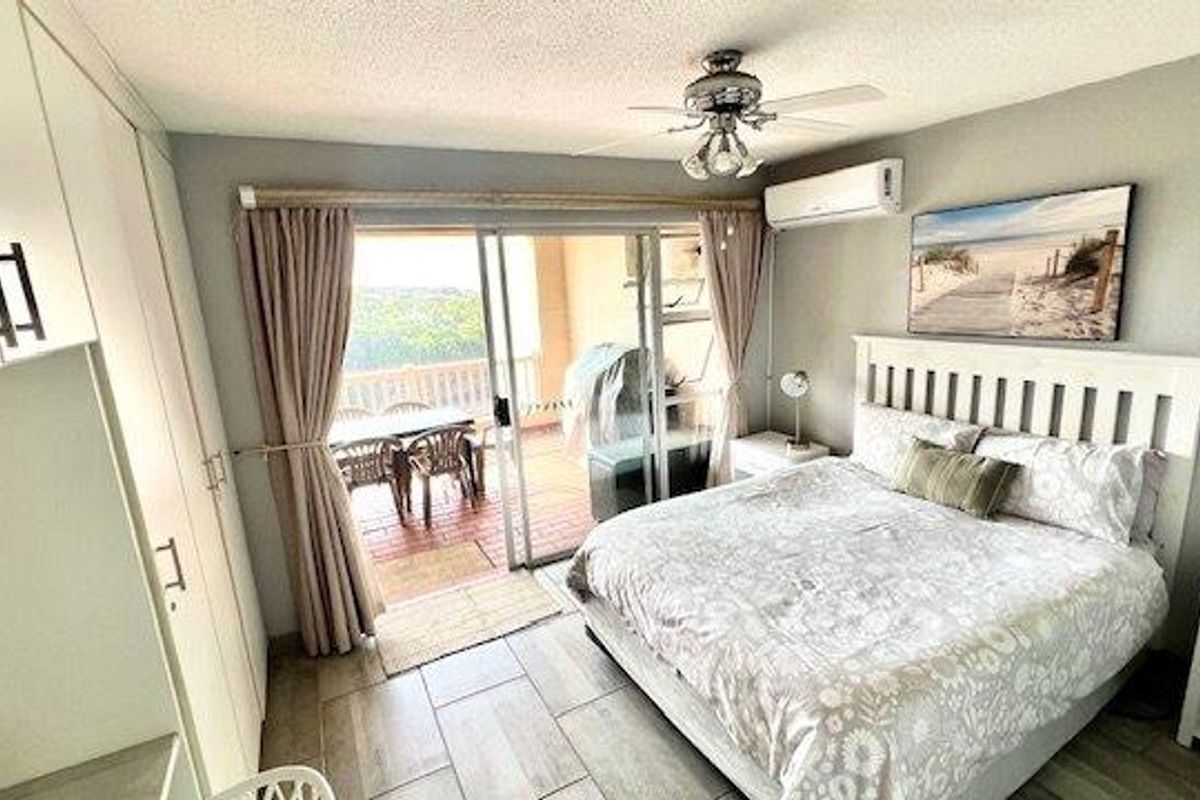 A well-maintained bedroom featuring built-in cupboards, a ceiling fan, air conditioning, and direct access to a private balcony through sliding glass doors.