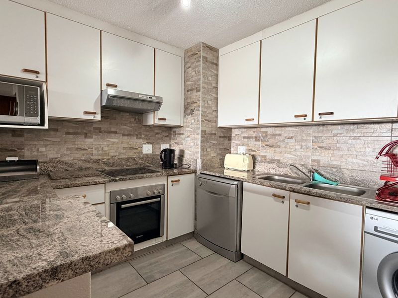 Functional kitchen featuring granite countertops, stone tile backsplash, built-in cabinetry, and integrated appliances including an oven, hob, and extractor fan.