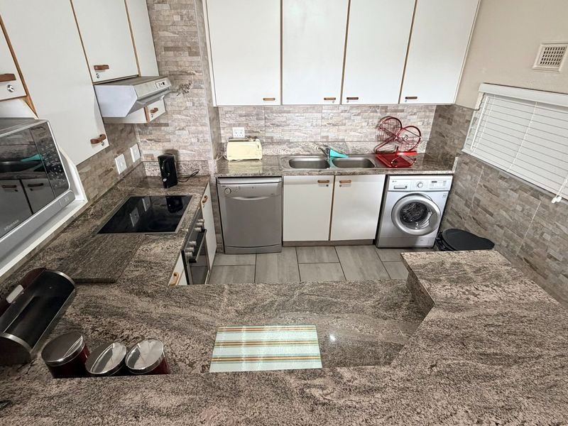 A well-appointed kitchen featuring granite countertops, built-in cabinetry, an electric hob with extractor, and integrated appliance connections for a dishwasher and washing machine.