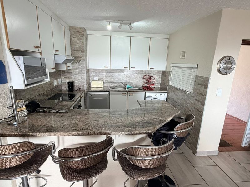 Functional kitchen featuring granite countertops, stone tile backsplash, built-in cabinetry, and integrated appliances with a breakfast bar layout.