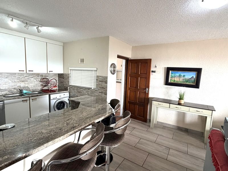 Open-plan kitchen featuring granite countertops, tiled flooring, and built-in cabinetry, seamlessly flowing into the living area.