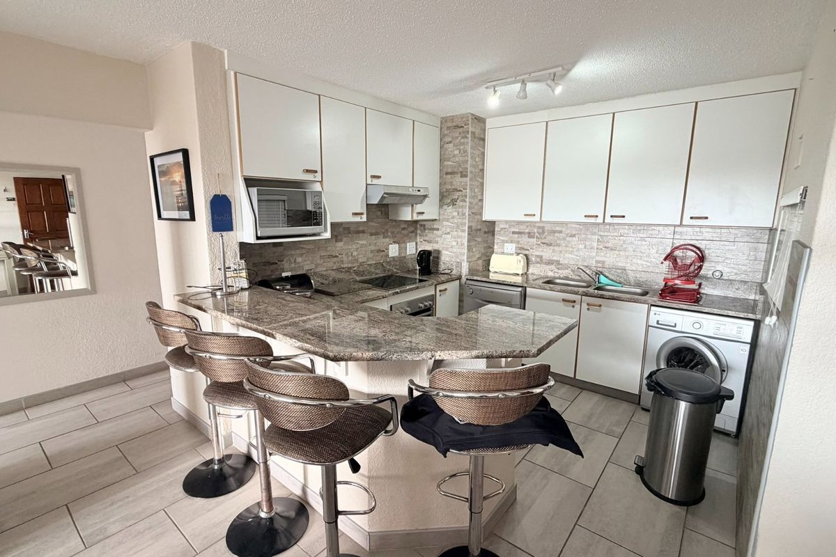 A functional kitchen featuring granite countertops, stone tile backsplash, built-in cabinetry, and integrated appliances with a breakfast bar area.