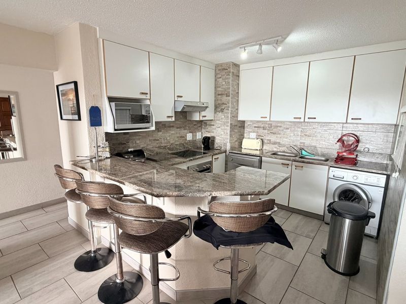 A functional kitchen featuring granite countertops, stone tile backsplash, built-in cabinetry, and integrated appliances with a breakfast bar area.