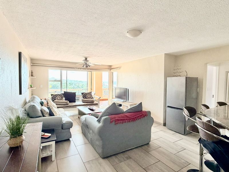 Spacious open-plan living and dining area featuring tiled flooring, a ceiling fan, and large sliding doors leading to an outdoor balcony.