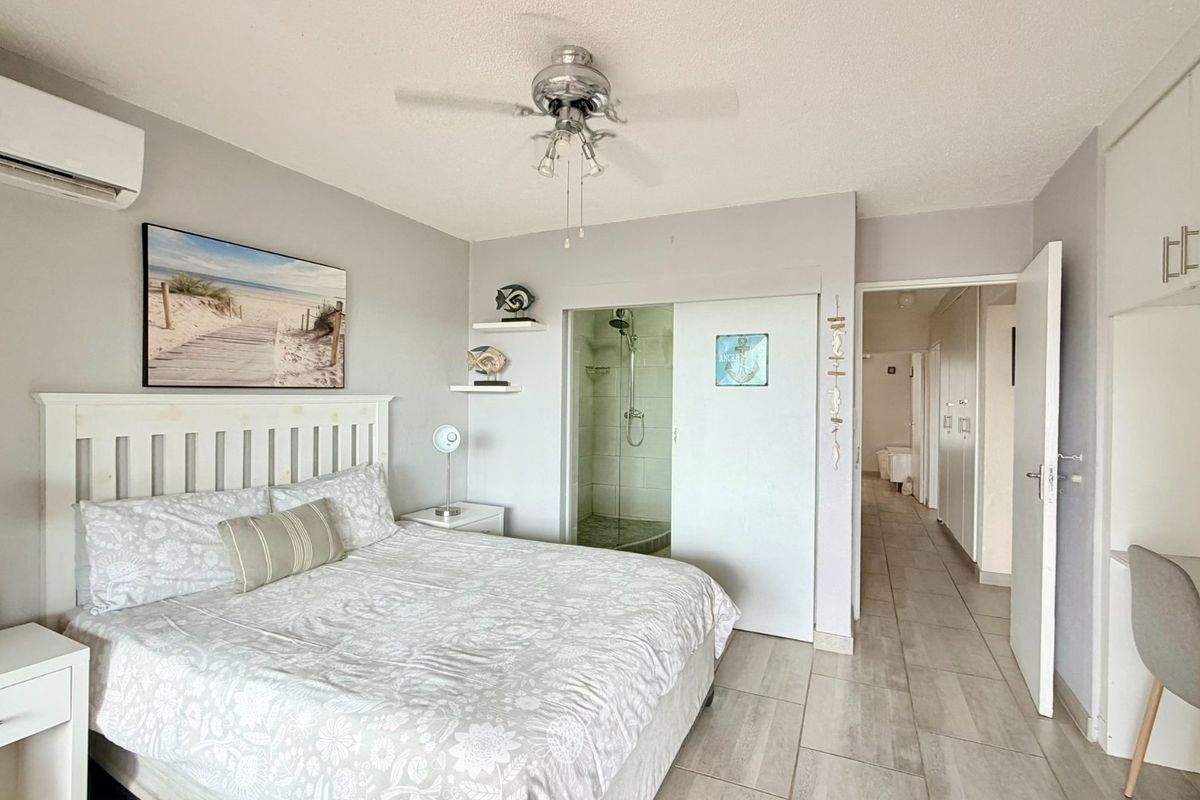 A well-maintained bedroom featuring tiled flooring, a ceiling fan, split-system air conditioning, and an en-suite shower room with sliding door access.