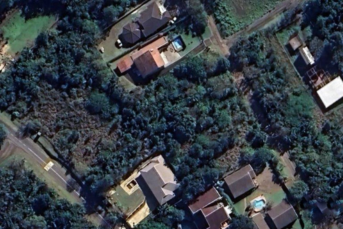 An aerial view of a residential area featuring established vegetation, surrounding homes, and local road access.