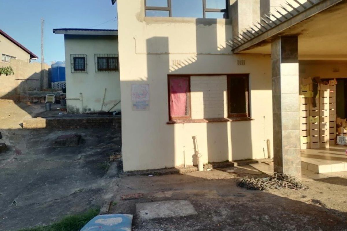 Rear exterior view of the property showing a paved courtyard area, concrete pillars, and multi-level building structure with visible exterior wall wear.