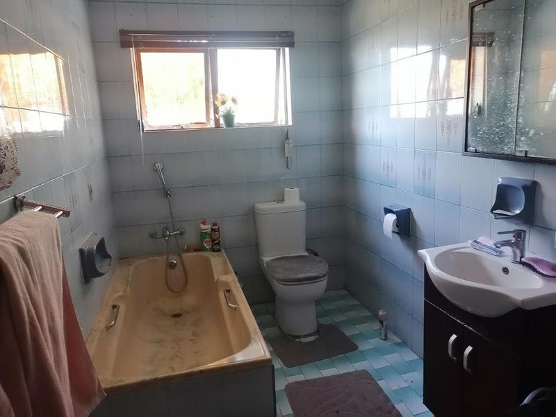 A dated bathroom featuring a bathtub, toilet, and vanity basin with wall-to-wall tiling and a window for natural light.
