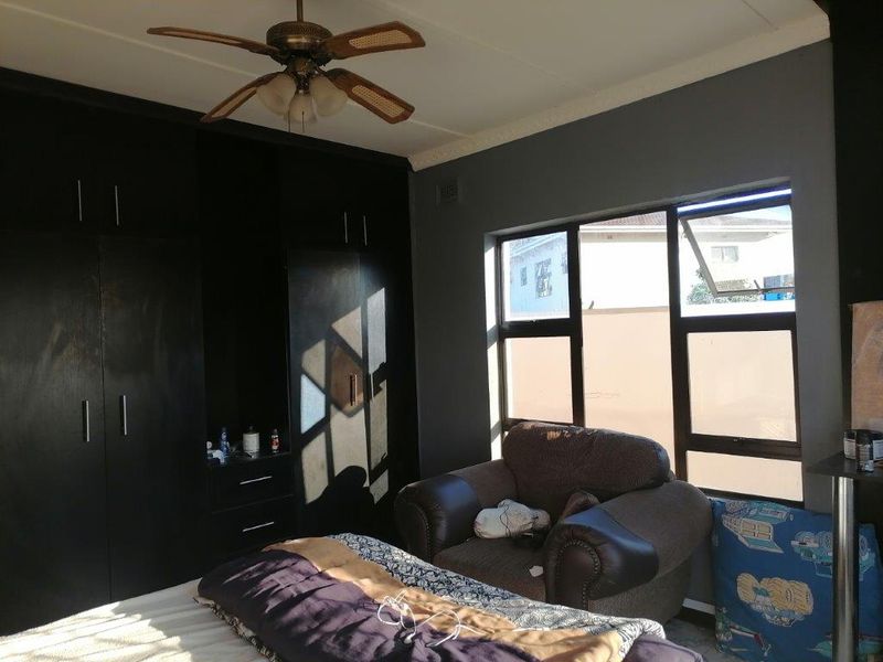 A bedroom featuring dark built-in cabinetry, a ceiling fan, and large windows allowing natural light into the space.