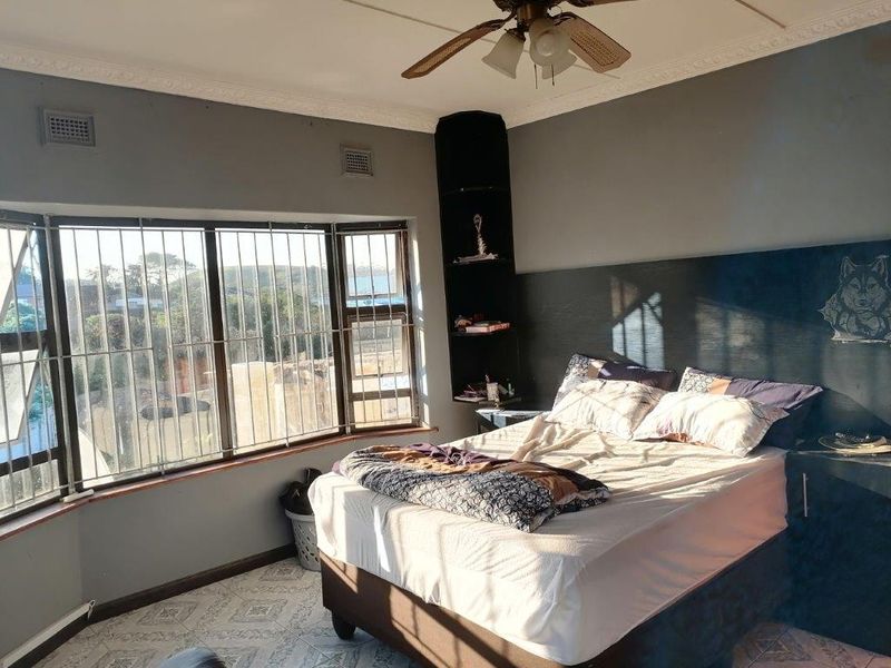 A bedroom featuring a large bay window with security bars, a ceiling fan, and built-in corner shelving.