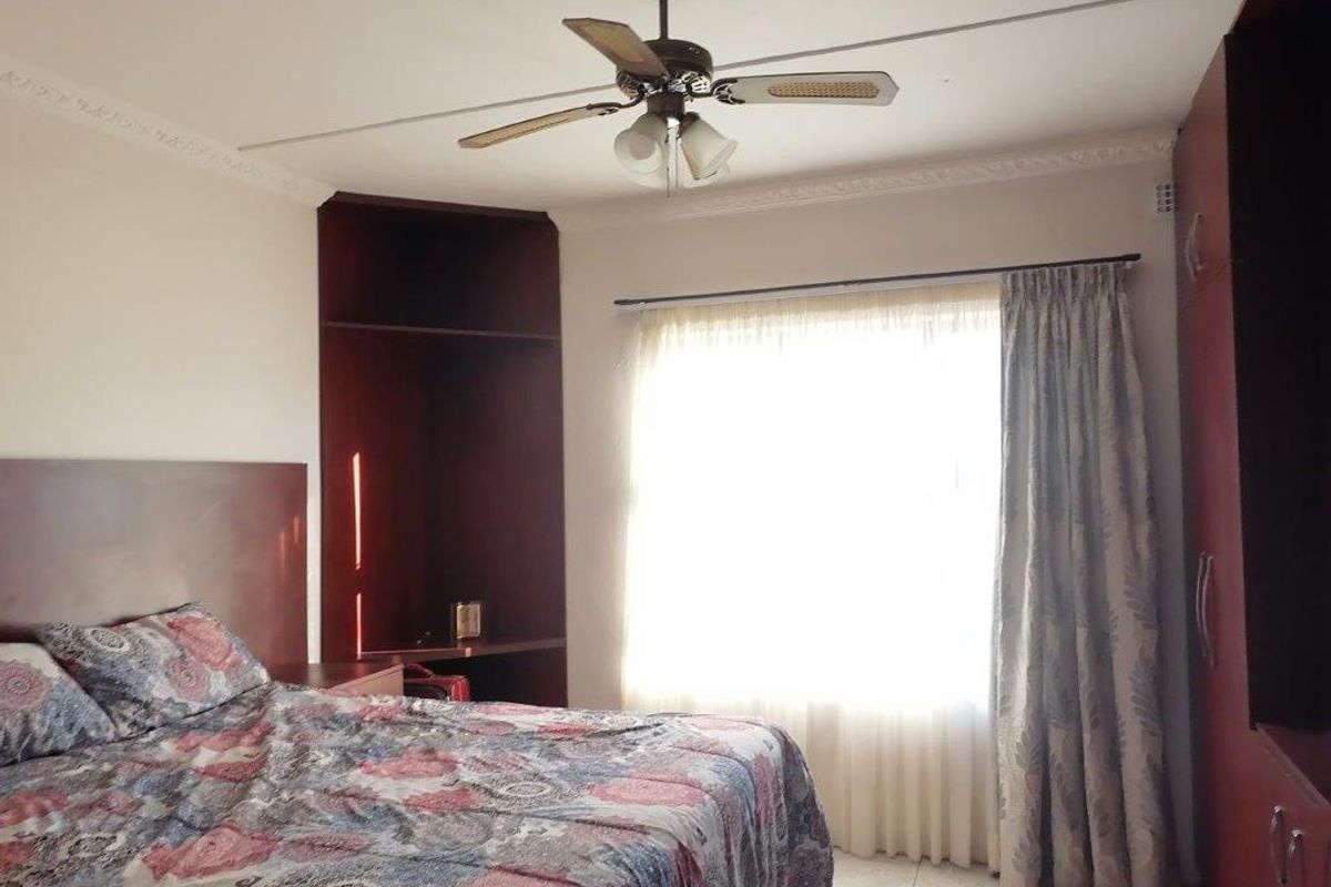 A bedroom featuring built-in dark wood cabinetry, a ceiling fan, and tiled flooring with natural light from the window.