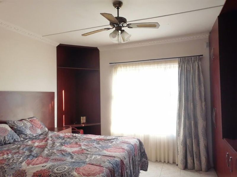 A bedroom featuring built-in dark wood cabinetry, a ceiling fan, and tiled flooring with natural light from the window.
