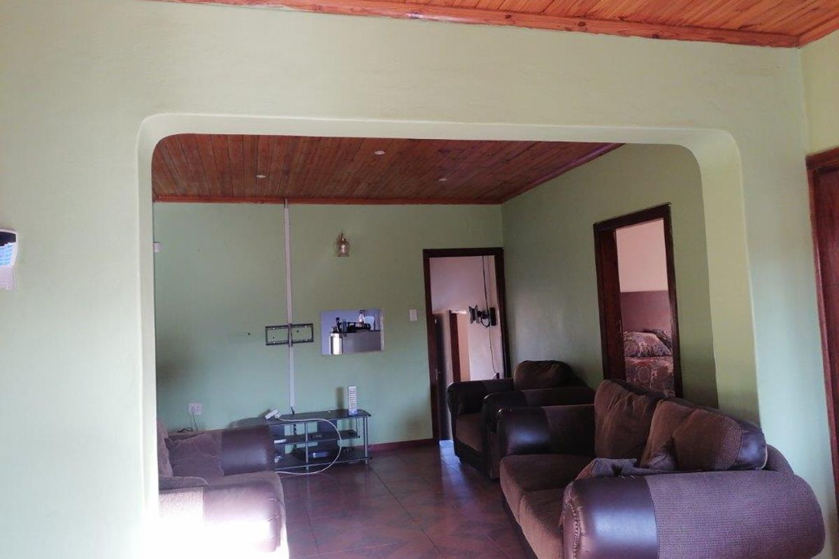 A living room featuring a timber-paneled ceiling, tiled flooring, and an arched transition leading to an adjacent space.