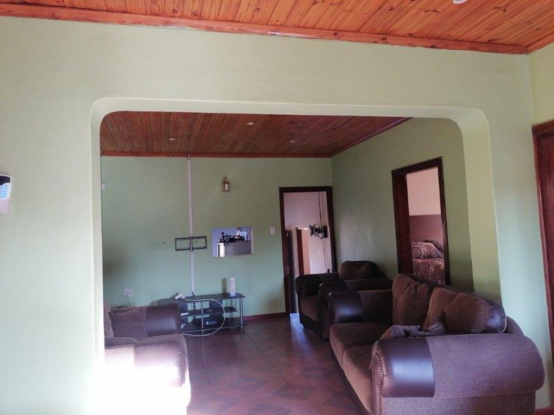A living room featuring a timber-paneled ceiling, tiled flooring, and an arched transition leading to an adjacent space.