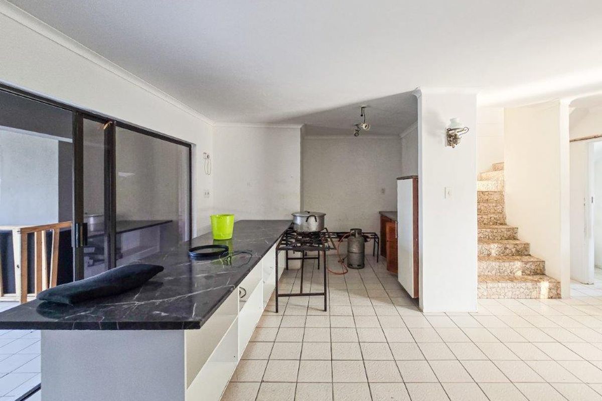 An open-plan kitchen area featuring a long stone-look countertop, tiled flooring, and direct access to an adjacent staircase and outdoor patio area.