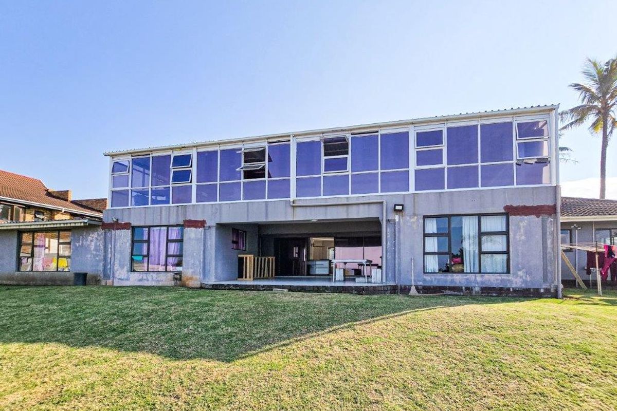 Rear view of a two-story house featuring extensive glass paneling, a covered patio area, and a large lawn.