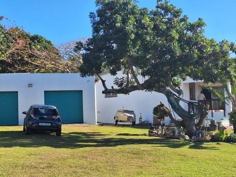 Front view of the property featuring a double garage with roller shutter doors and a covered porch area set within a spacious garden.