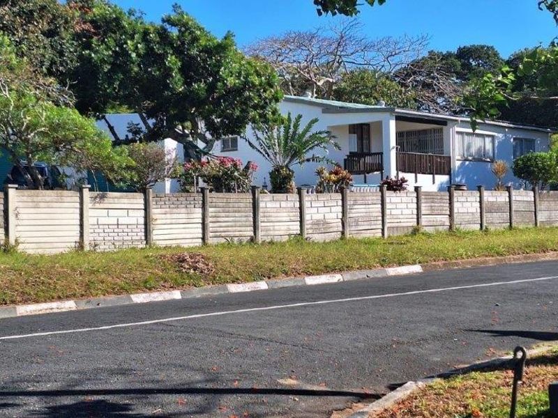 Street view of the property featuring a precast concrete boundary wall, a covered patio, and established garden surroundings.