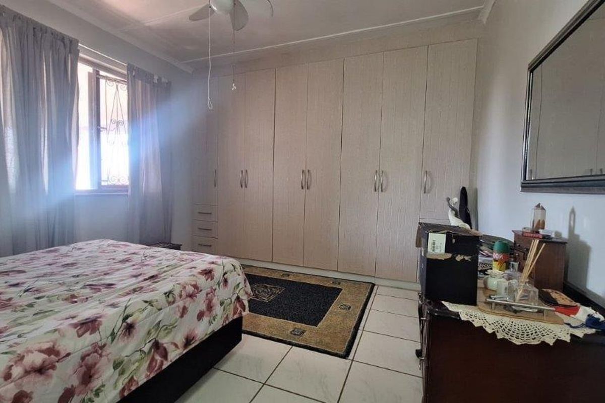 A bedroom featuring built-in cupboards, tiled flooring, and a ceiling fan, offering a functional space with natural light.