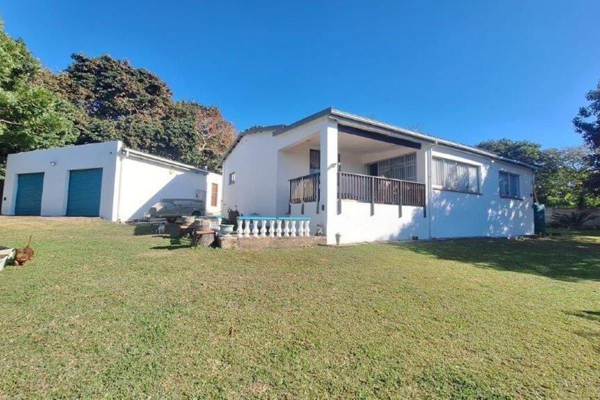 Rear view of the property featuring a covered patio, lawn area, and a detached garage with roller shutter doors.