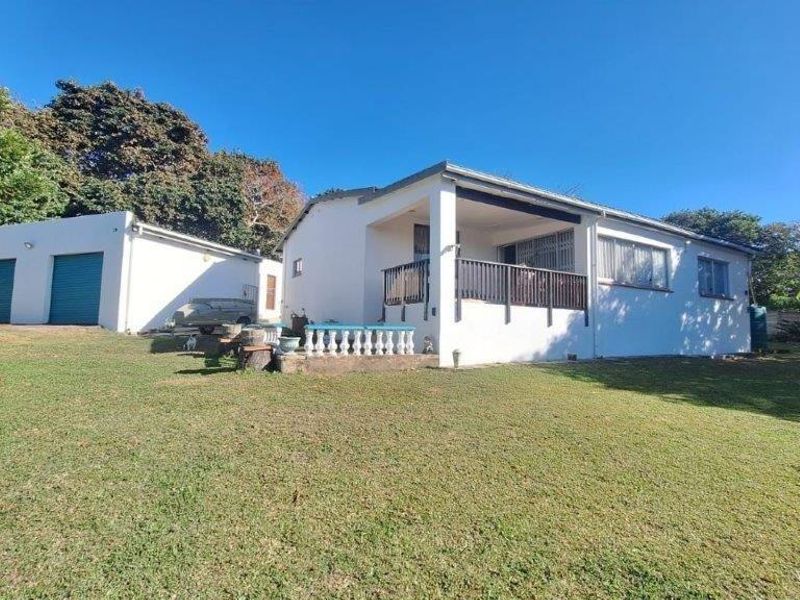 Rear view of the property featuring a covered patio, lawn area, and a detached garage with roller shutter doors.