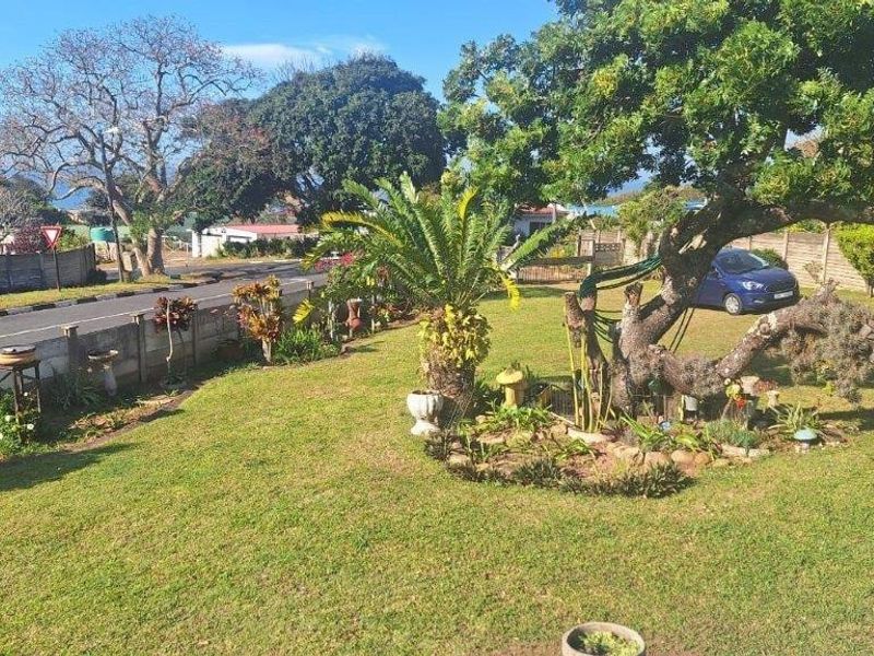A spacious front garden featuring a well-maintained lawn, mature trees, and a precast concrete boundary wall bordering the street.