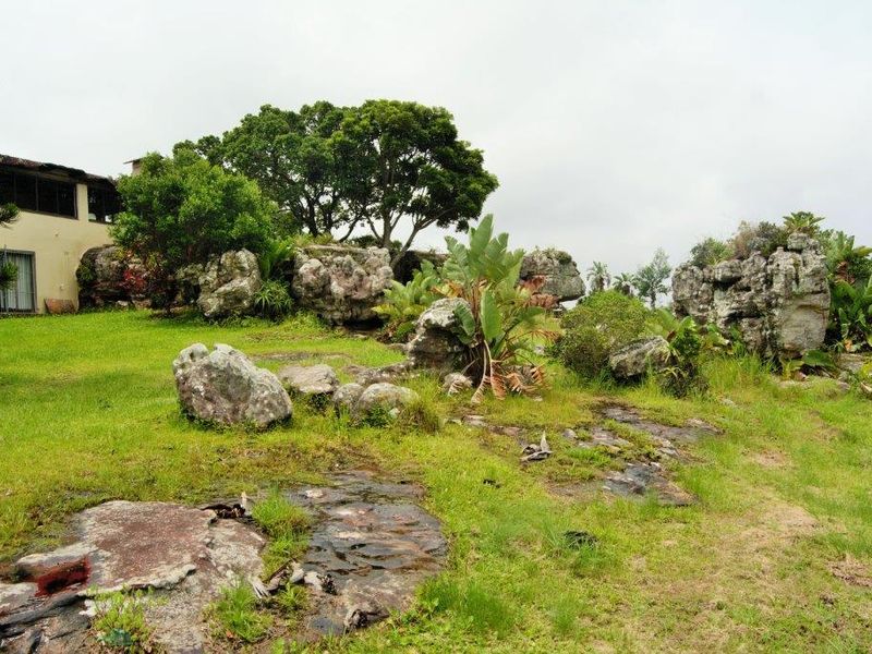 A spacious garden area featuring natural rock formations, mature trees, and a well-maintained lawn adjacent to the main property structure.